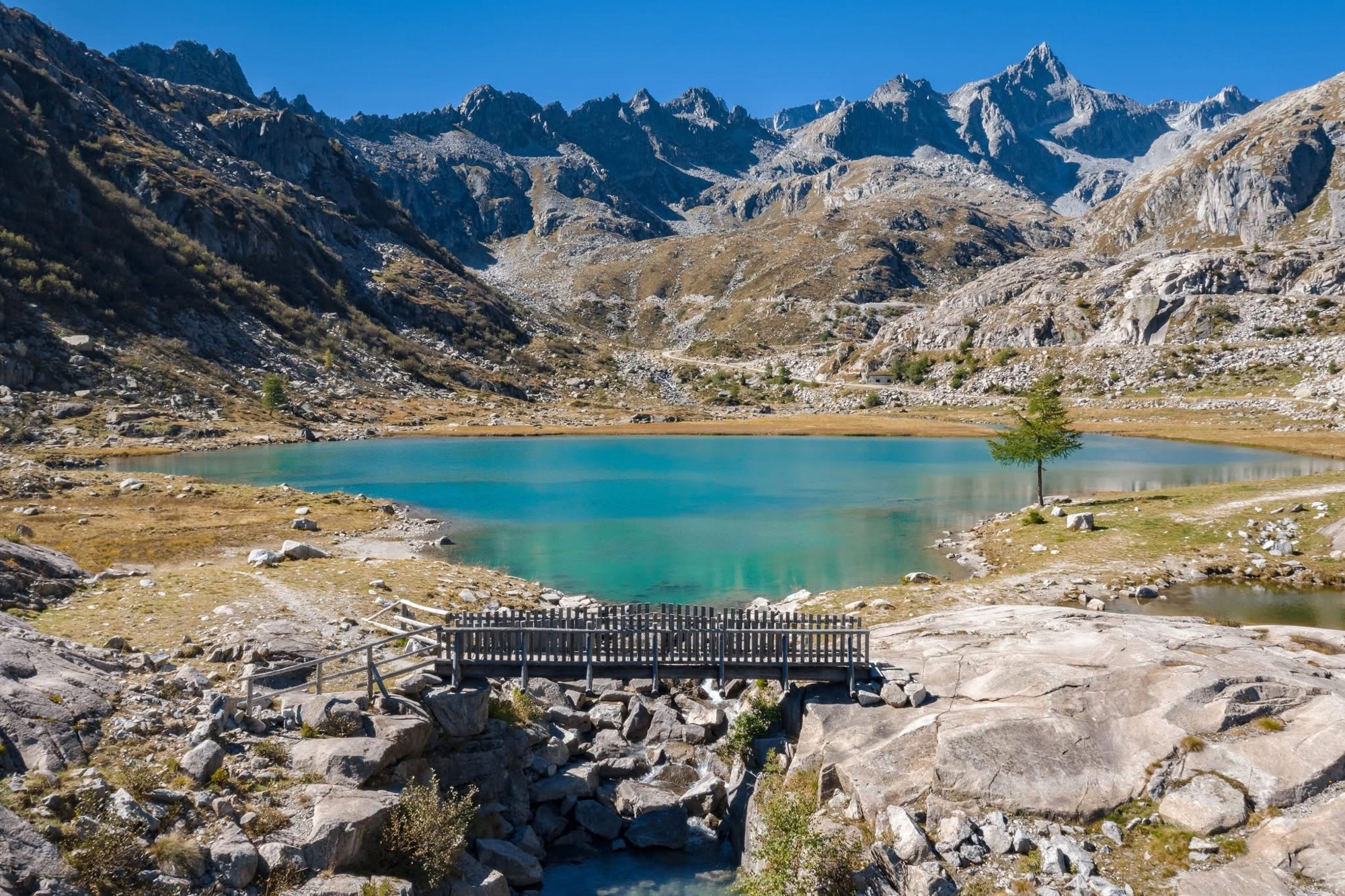 Lago alpino turchese tra le montagne del Trentino, con una passerella in legno